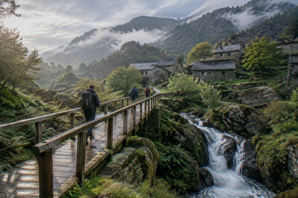 Hikers crossing a wooden bridge above a waterfall in a green mountain park