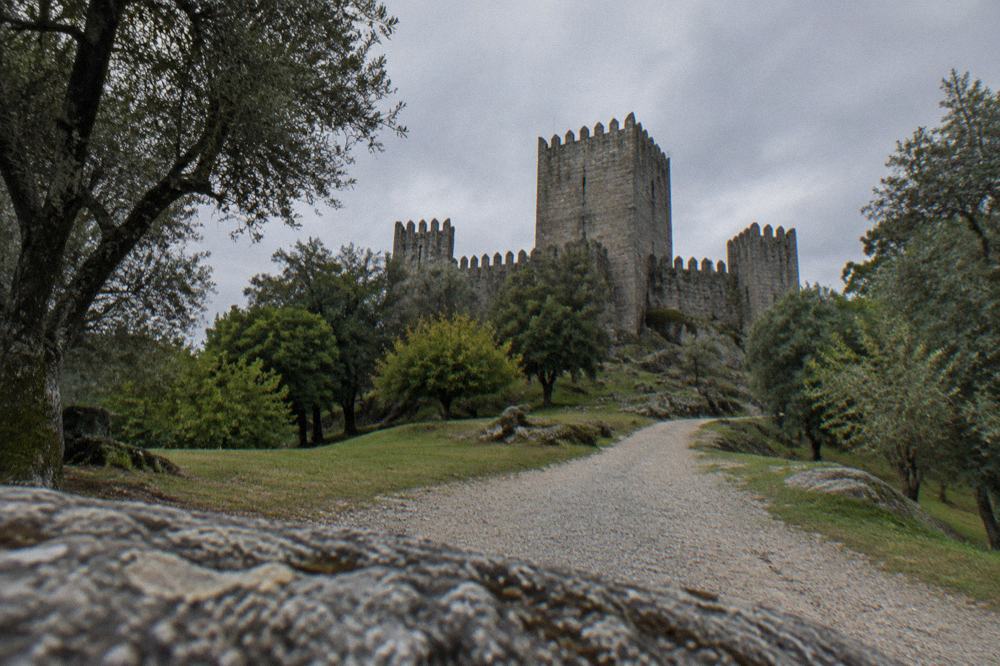 Stone walls and towers of a medieval castle rising above woodland in Guimaraes