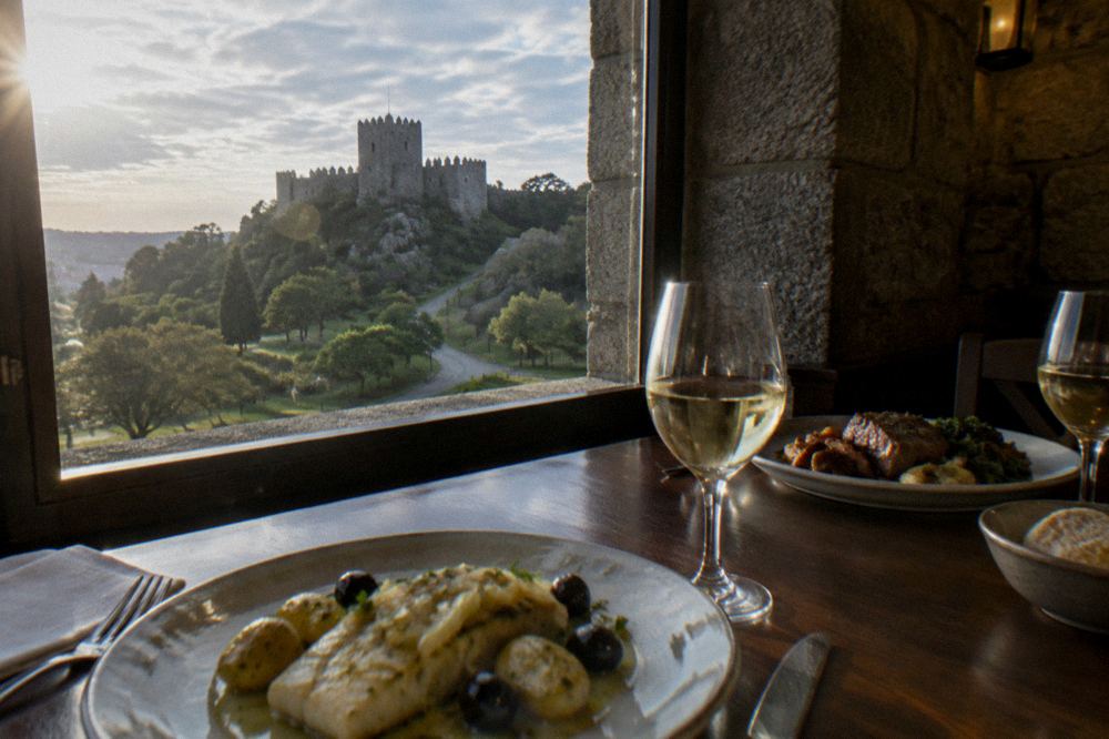 A restaurant table with codfish, roast meat and glasses of white wine in a stone-walled dining room