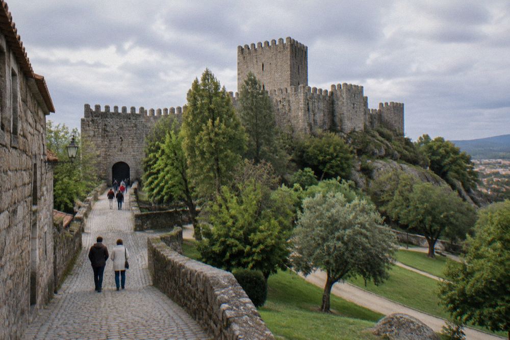 Visitors walking up a cobbled street towards a stone castle gate in warm afternoon light