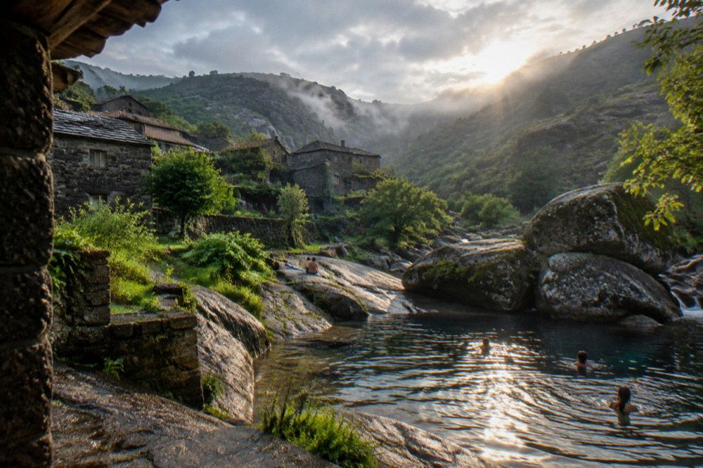 A clear river pool between rocks with people swimming at the edge