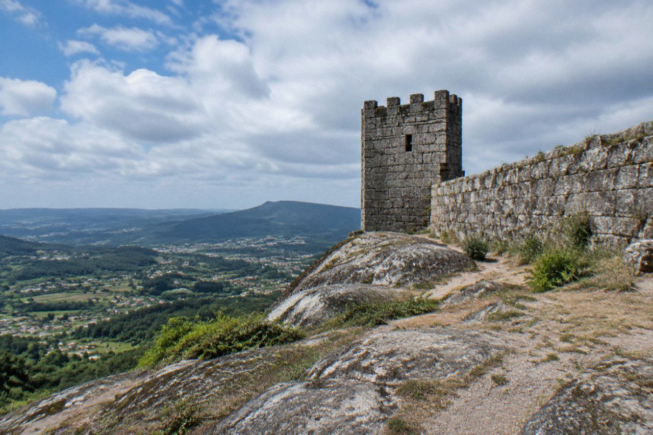 A medieval stone castle on a large granite outcrop above a green valley in northern Portugal