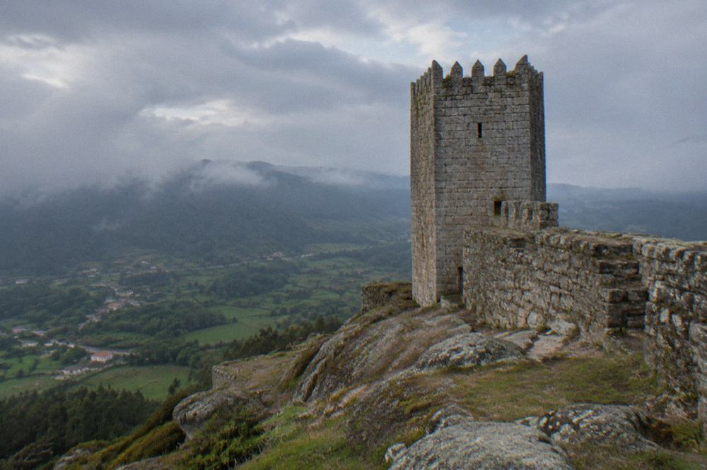 A granite castle tower seen from below against a partly cloudy sky