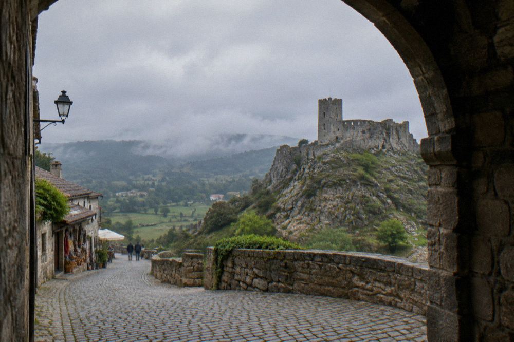 A stone archway in a historic Portuguese town with cobbled street and small shops