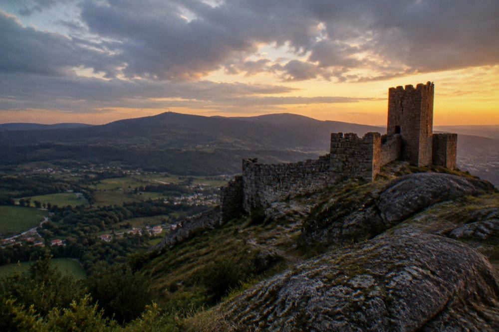 A granite hilltop keep silhouetted against a golden evening sky over green fields