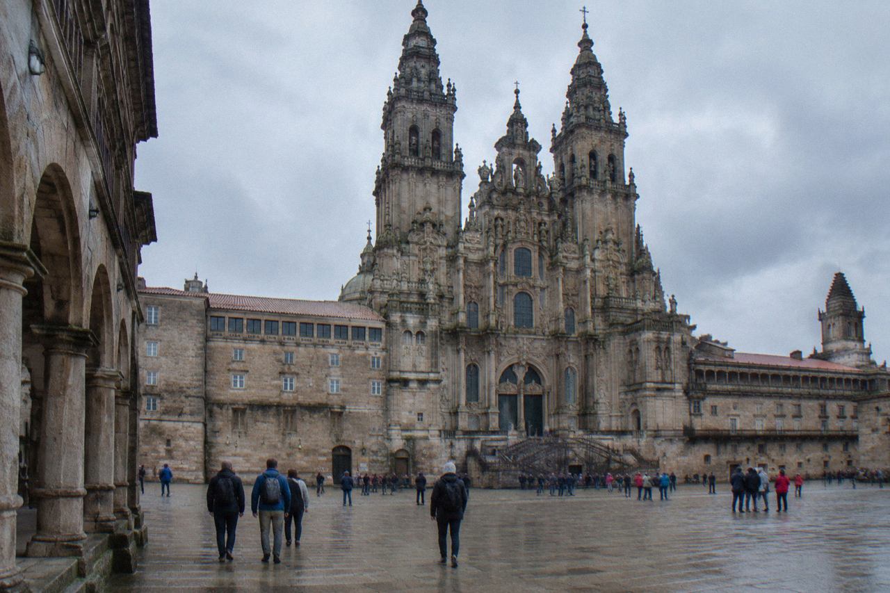 The baroque facade of Santiago de Compostela cathedral rising above a wide stone square with pilgrims and visitors gathered in front