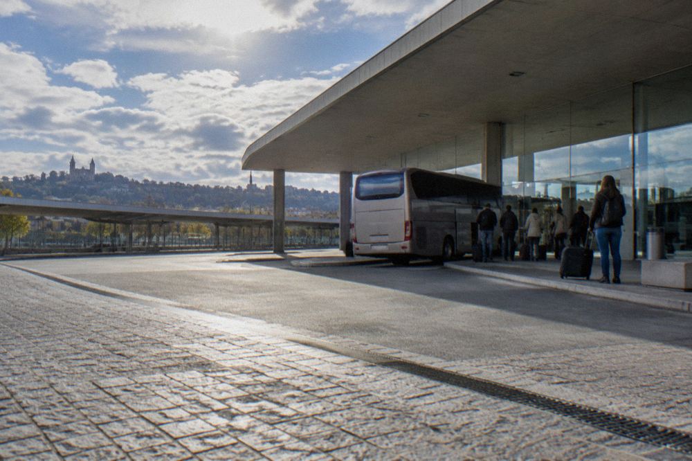 A long-distance coach parked at a covered bus station bay with passengers waiting with luggage