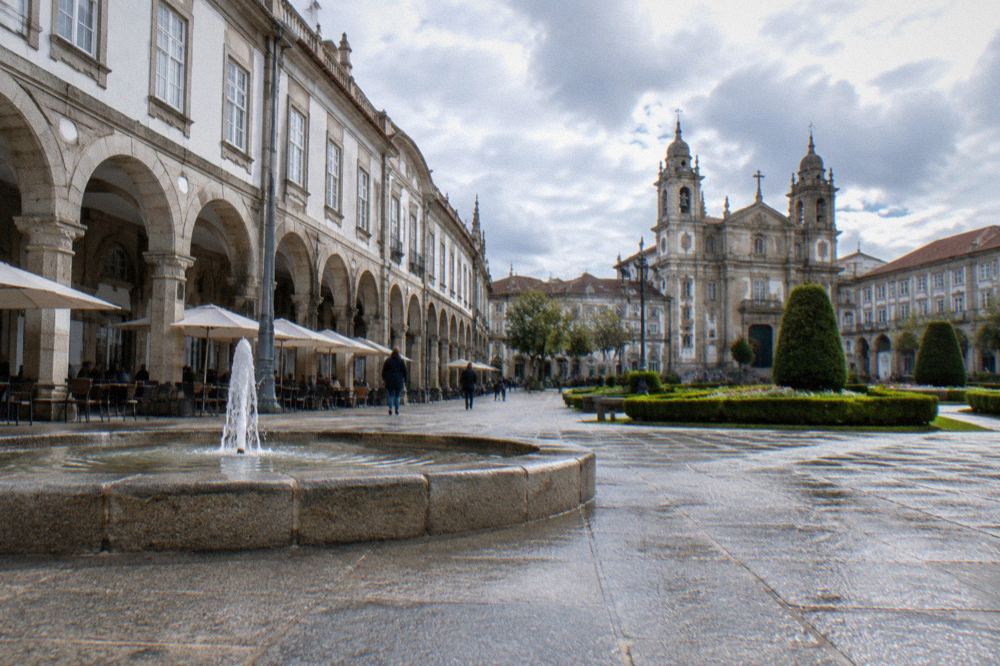A narrow granite-paved street in Santiago's old town with arcaded buildings and café tables along the walls
