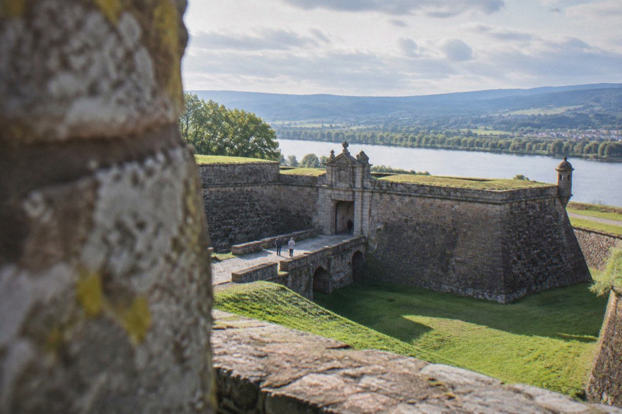 Stone fortress walls of a hilltop town rising above a wide green river