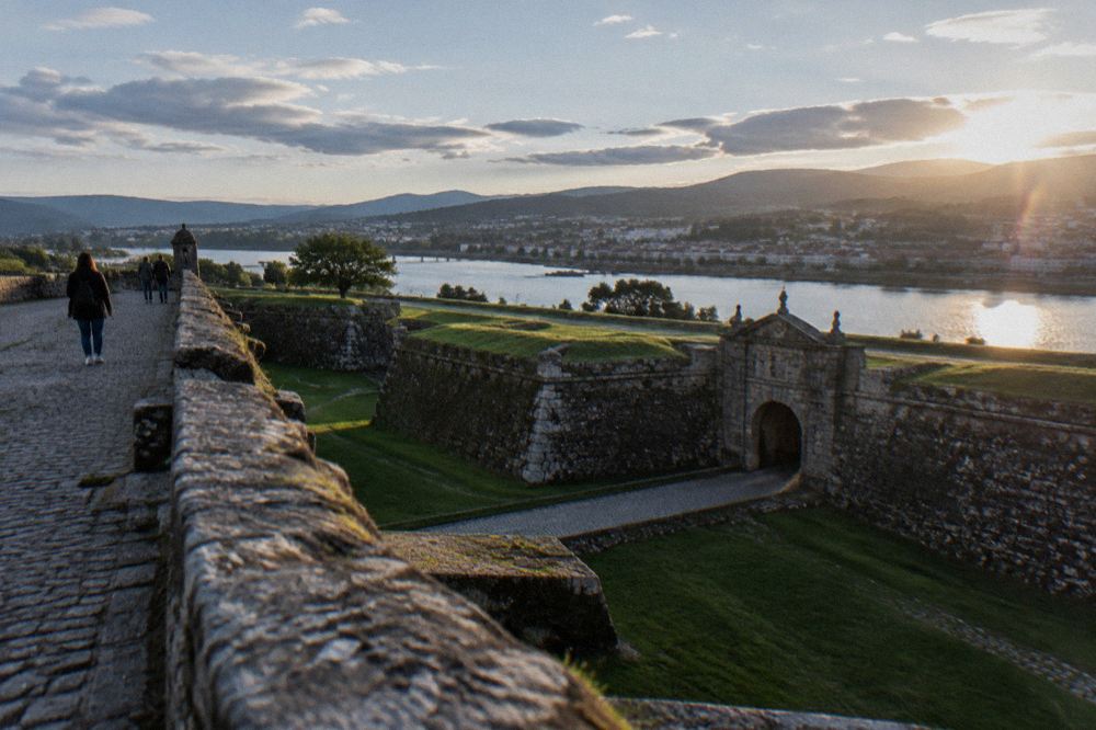 Walkers on a wide stone rampart path with views over a river and a town on the far bank