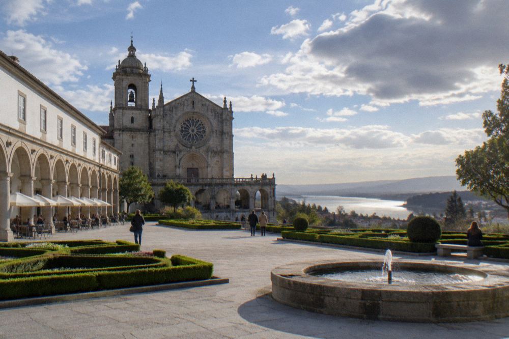 Stone basilica with a rose window and arcaded terrace overlooking a river estuary and coastline