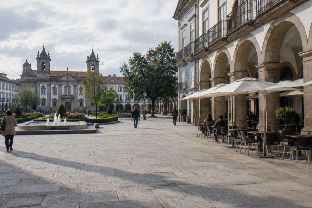 Arcaded town square with granite paving, cafe tables and tiled building facades in afternoon sun