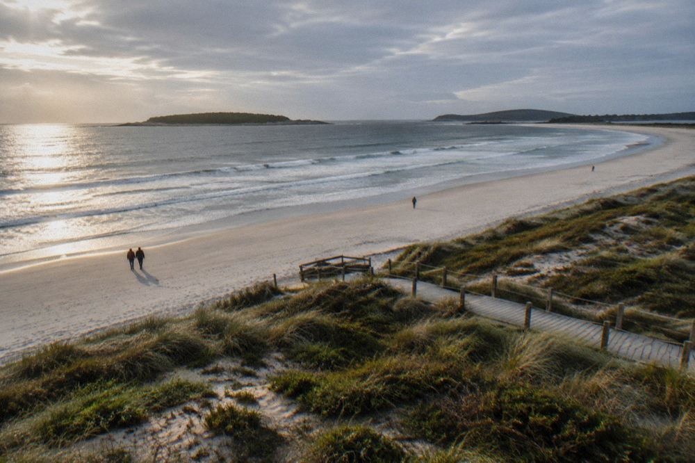 A curved white sand beach between two green islands with turquoise water