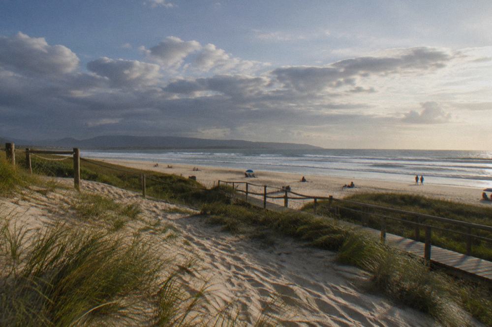 Sunbathers on golden sand under a clear blue summer sky with breaking waves behind