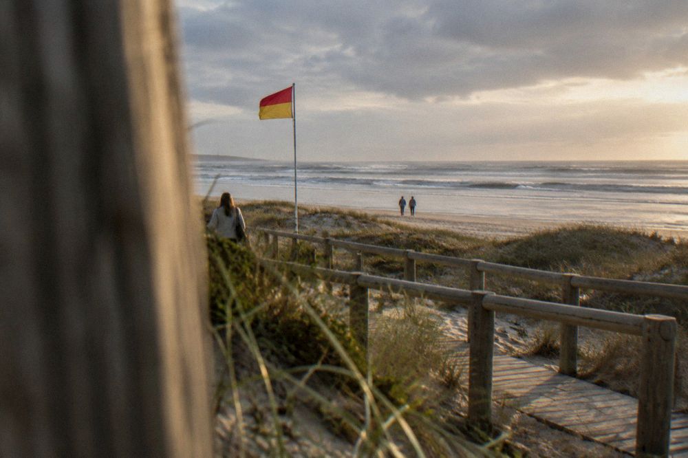 Red and yellow lifeguard flag flying above a sandy beach with wooden walkways over the dunes