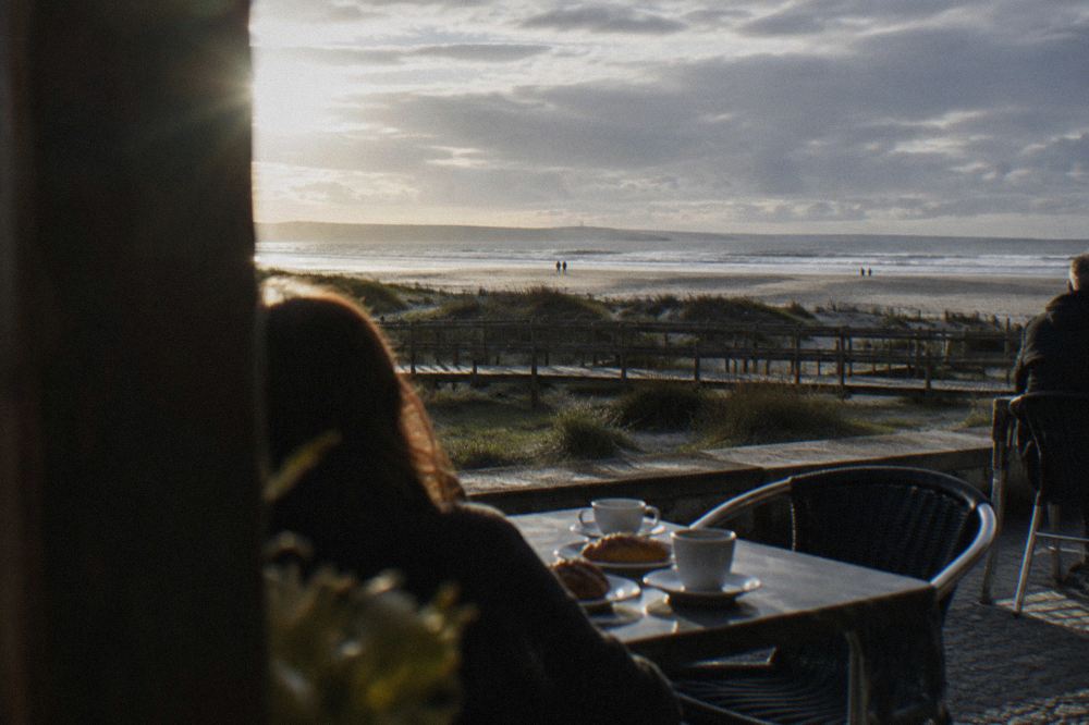 Outdoor cafe tables on a seafront promenade with white coffee cups and pastries in the sun