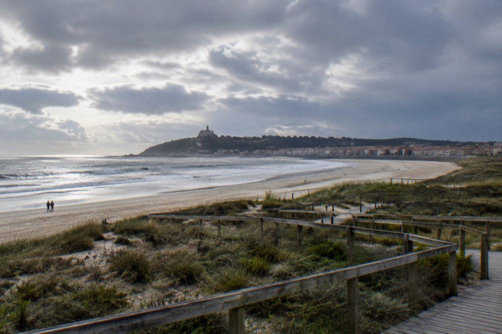 Wide sandy bay curving below a hilltop sanctuary with a historic town of granite squares in the foreground