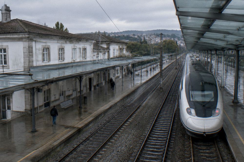 A high-speed train waiting at a Lisbon station platform under a glass canopy
