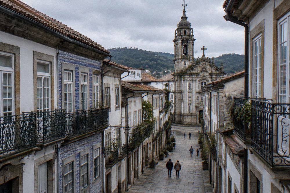 A quiet Braga street in morning light with a baroque church tower rising above the rooftops