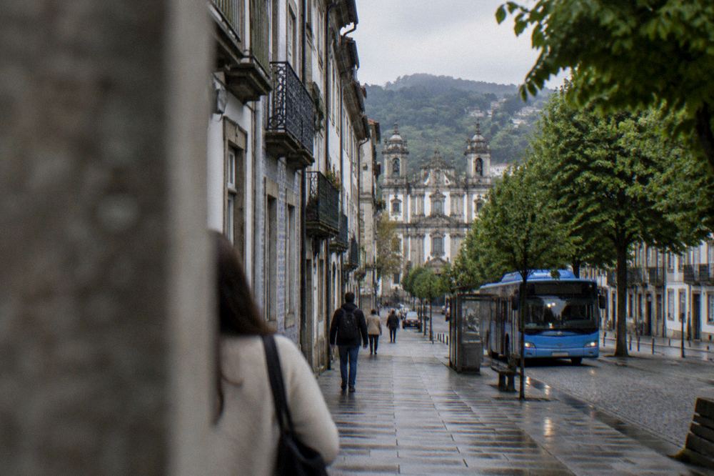 A blue city bus waiting at a stop on a tree-lined avenue in Braga