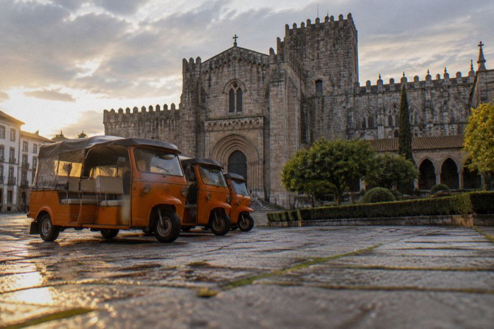 A row of orange tour tuk tuks parked near Braga's cathedral square