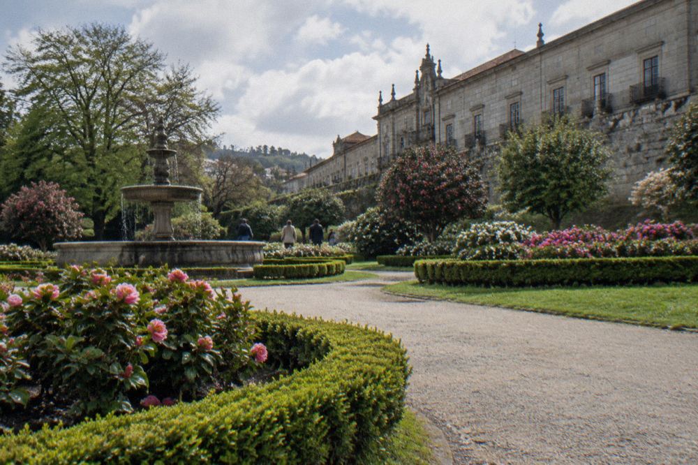 A gravel path curving through lawns and flowerbeds in a city park, with people strolling in the distance