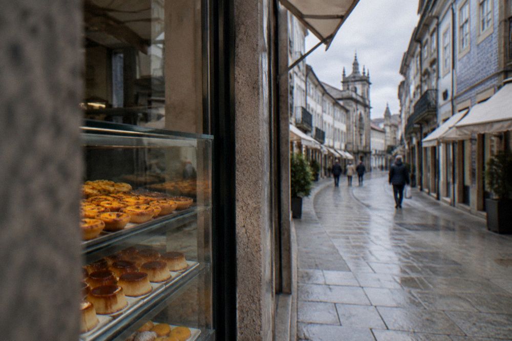 A glass display case filled with small golden egg-yolk pastries and caramel puddings in a pastry shop