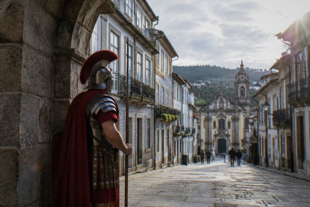 A reenactor in a Roman legionary costume standing beside a stone arch in a European old town