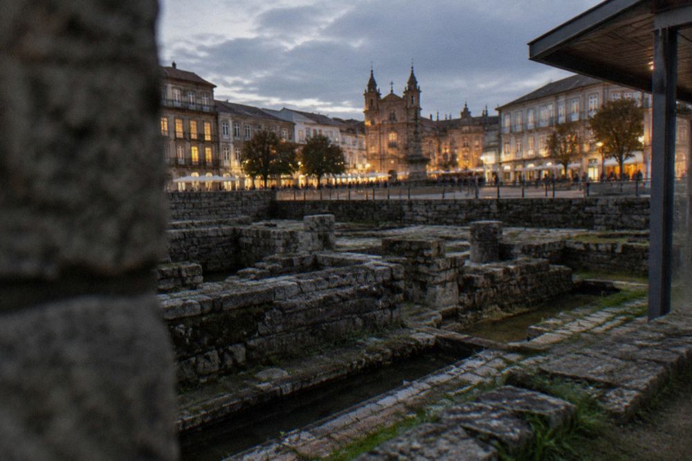 An illuminated European city square at dusk with crowds and historic facades