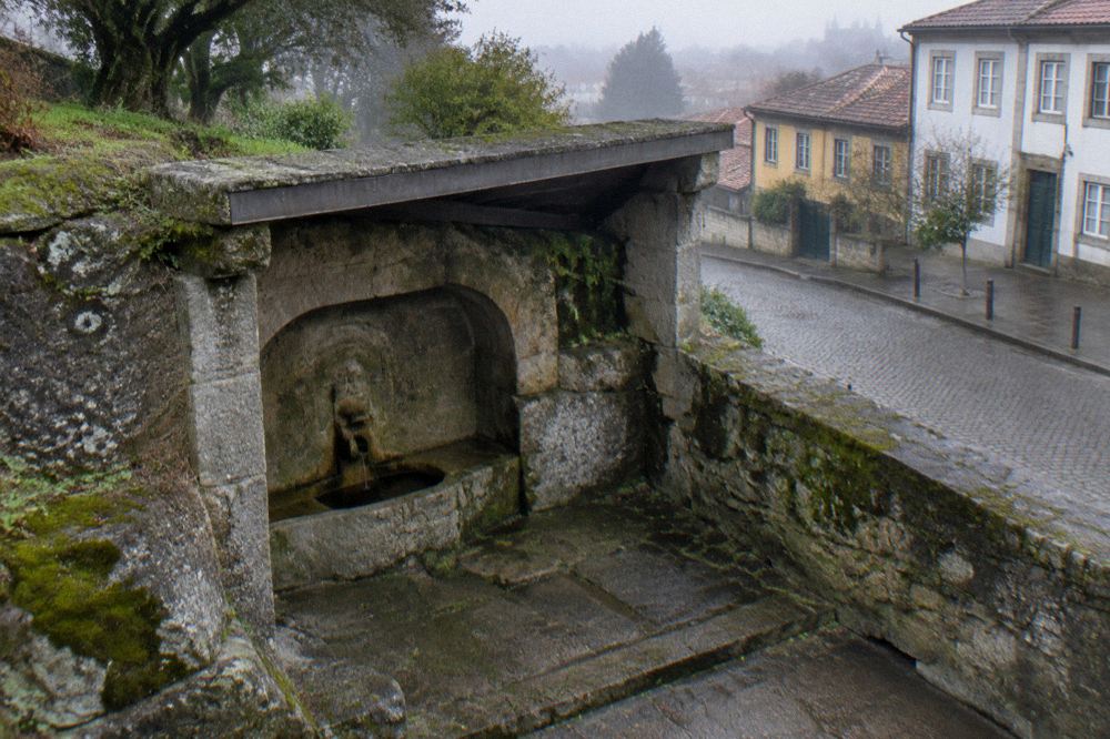 A stone Roman fountain carved into a rock face inside a small covered chamber