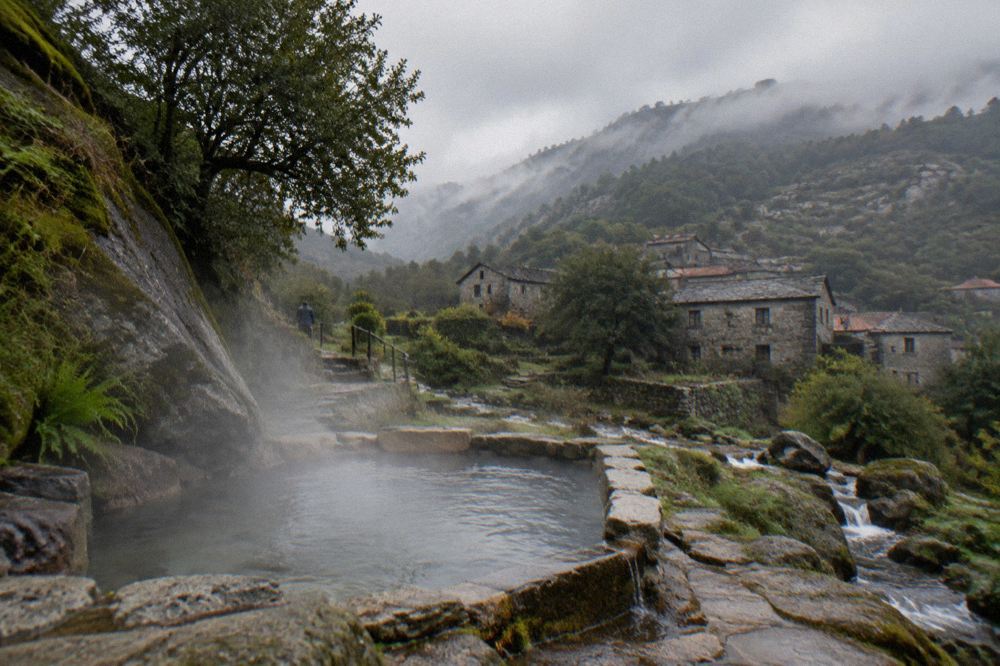 Steam rising gently from a stone thermal pool surrounded by green mountains