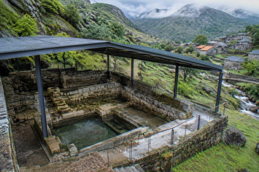 Ancient Roman stone bath structures viewed under a modern protective roof