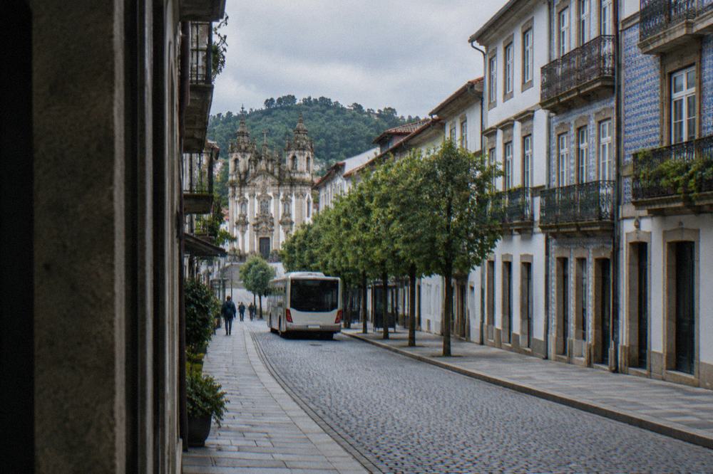 A city bus pulling away from a stop on a tree-lined avenue in Braga