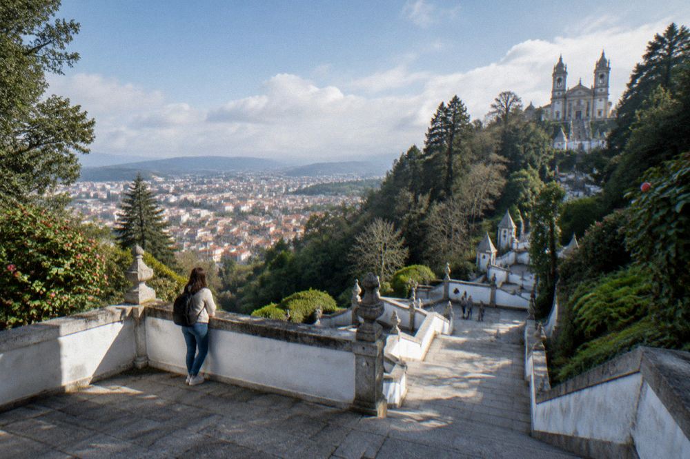 A walker pausing on a stone landing of the Bom Jesus stairway with the city spread out below