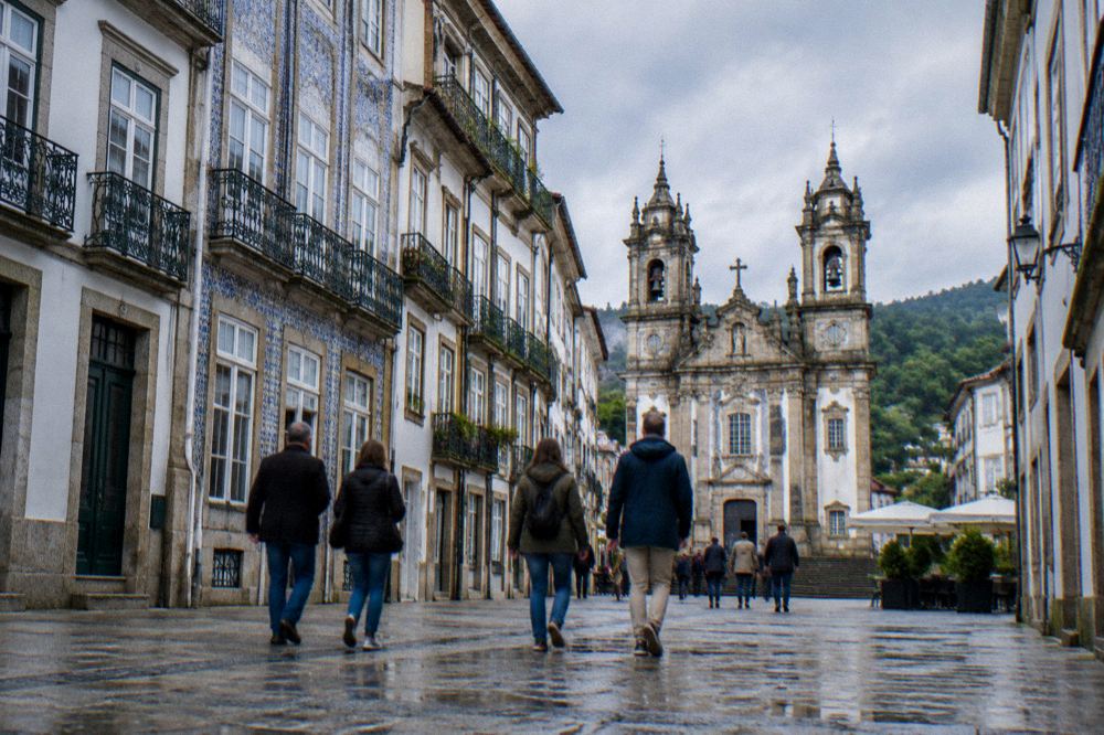 A walking group crossing a granite square in Braga with church towers behind