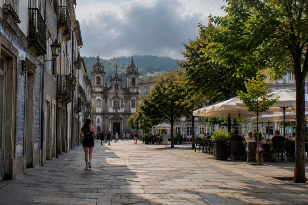 A sunny summer afternoon on a granite-paved square in Braga with cafe tables in the shade