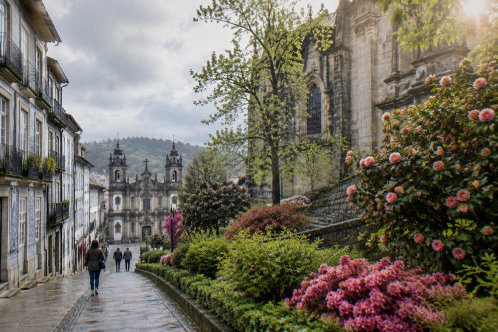 Spring flowers along a garden path below the walls of a historic Braga church