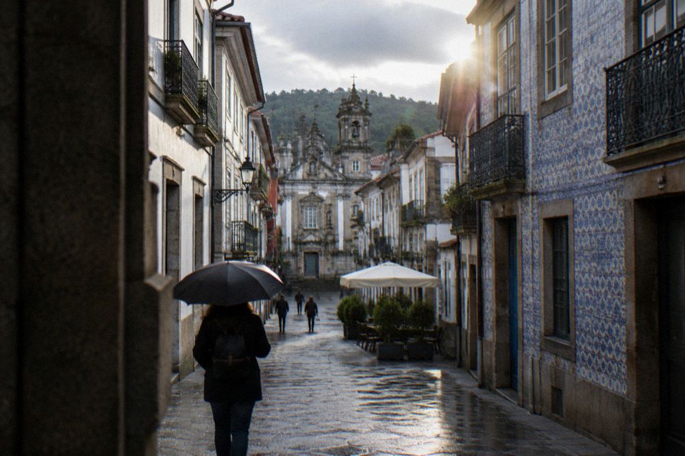 A traveller with a small backpack and umbrella walking a narrow street of old Braga