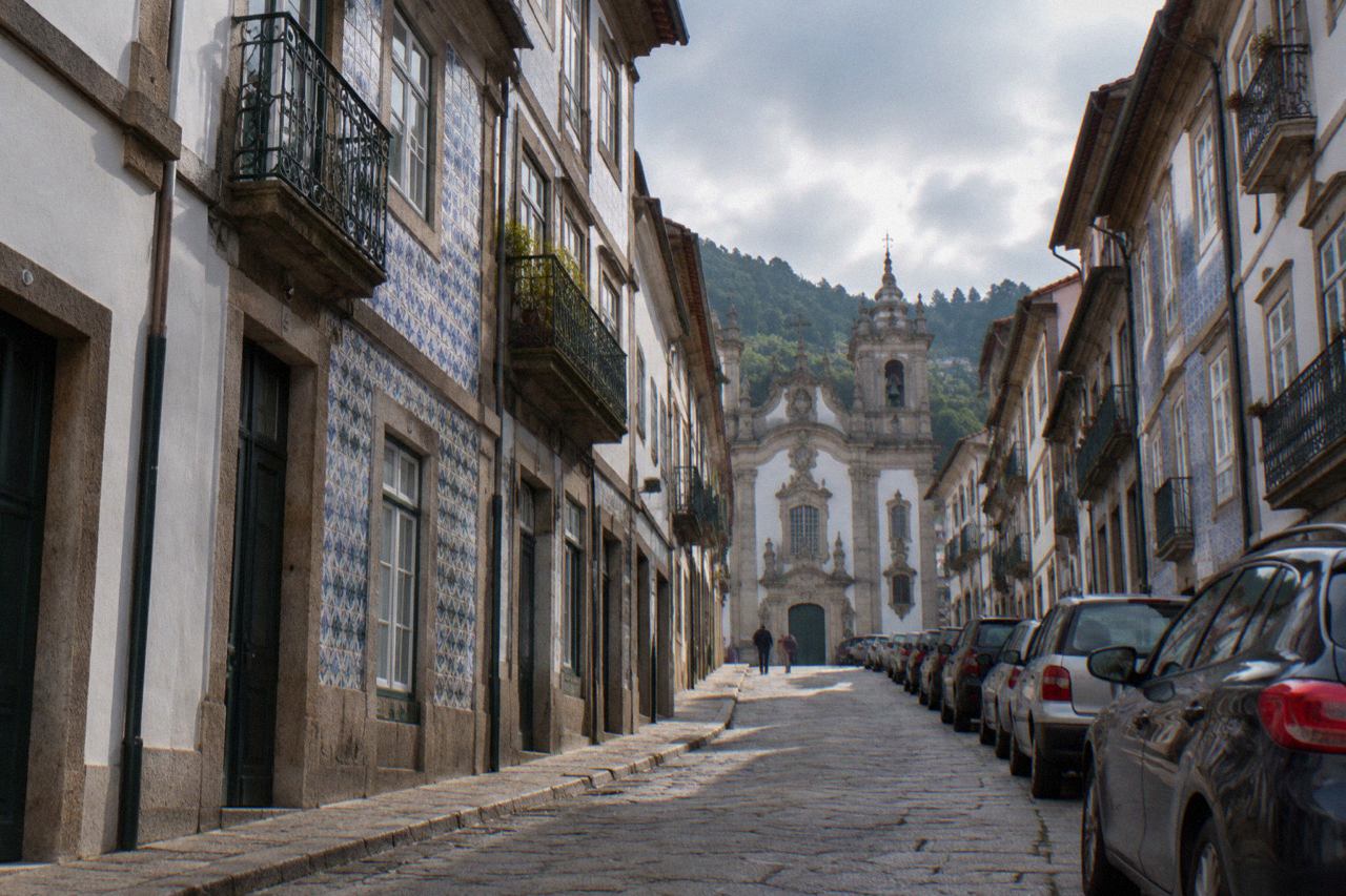A narrow street in Braga with parked cars along the kerb and historic buildings on both sides