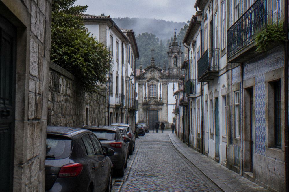 A narrow cobbled street in Braga with parked cars squeezed against old stone walls