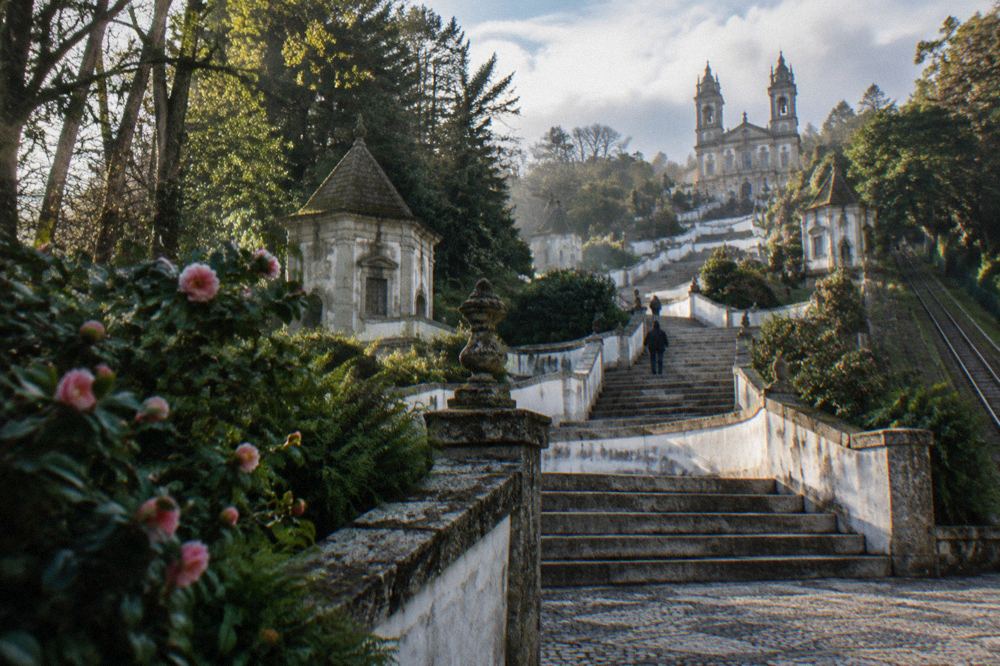 A wide stone staircase zigzagging up a wooded hillside lined with fountains and chapels