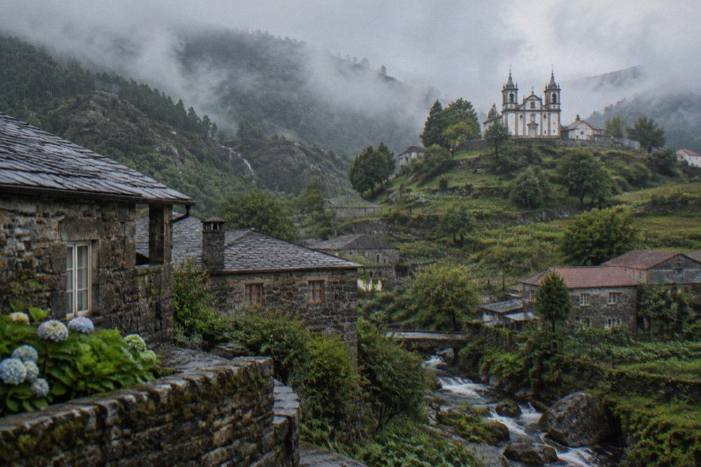 A white baroque church with twin bell towers standing on a green hilltop above farmland