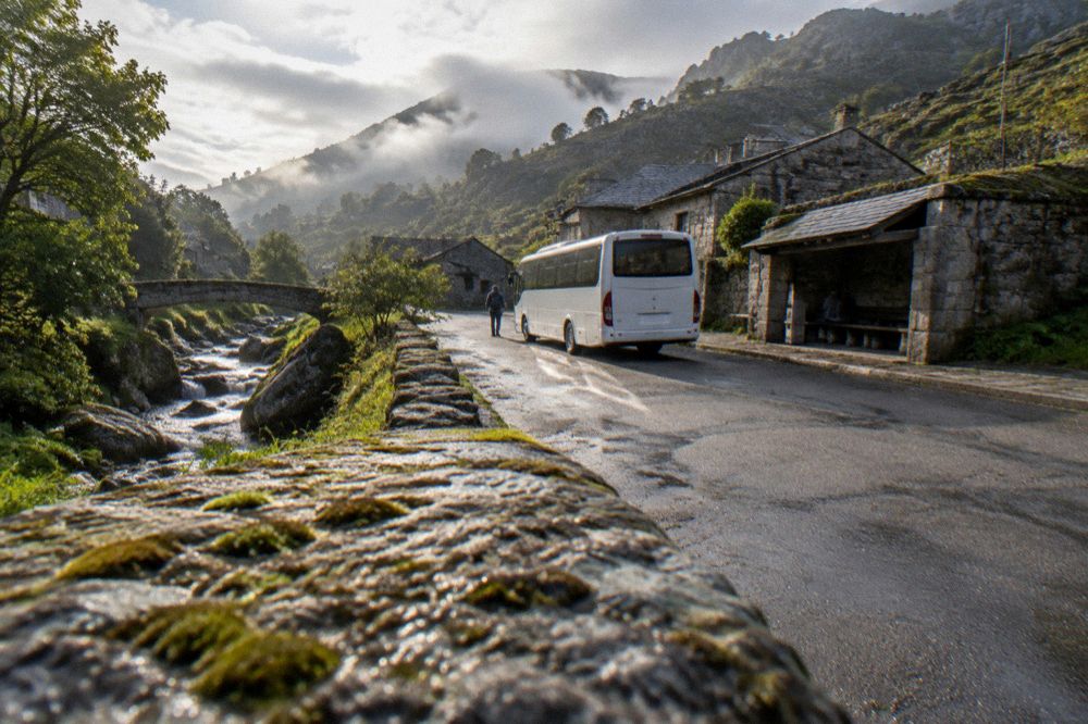 A white regional bus parked at a small stone village stop in a mountain valley