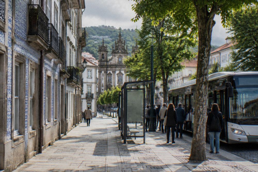 A city bus at a stop on a tree-lined street in Braga with passengers waiting to board