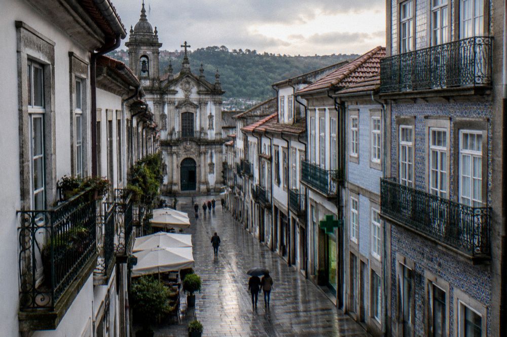 A pharmacy storefront with a green cross sign on a Braga street