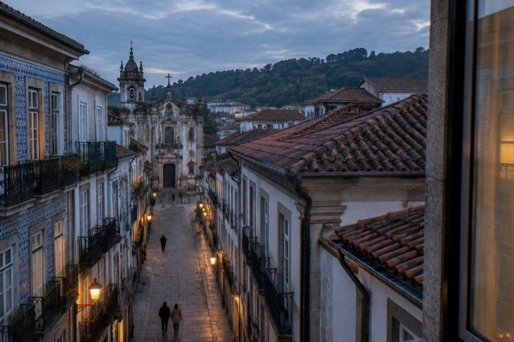 A hotel guest room window overlooking tiled rooftops of a Portuguese old town at dusk