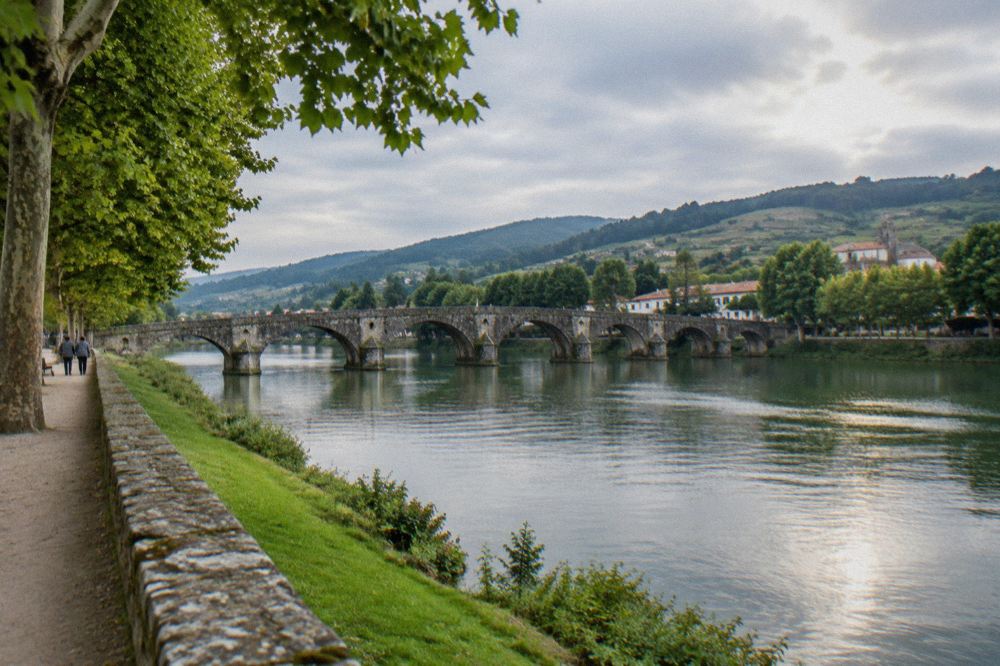 A stone Roman bridge arching over a calm green river between wooded banks