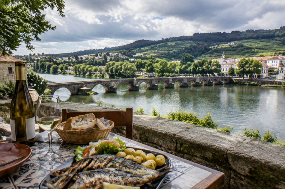 A rustic table with a bottle of white wine, grilled fish and bread in a tiled restaurant