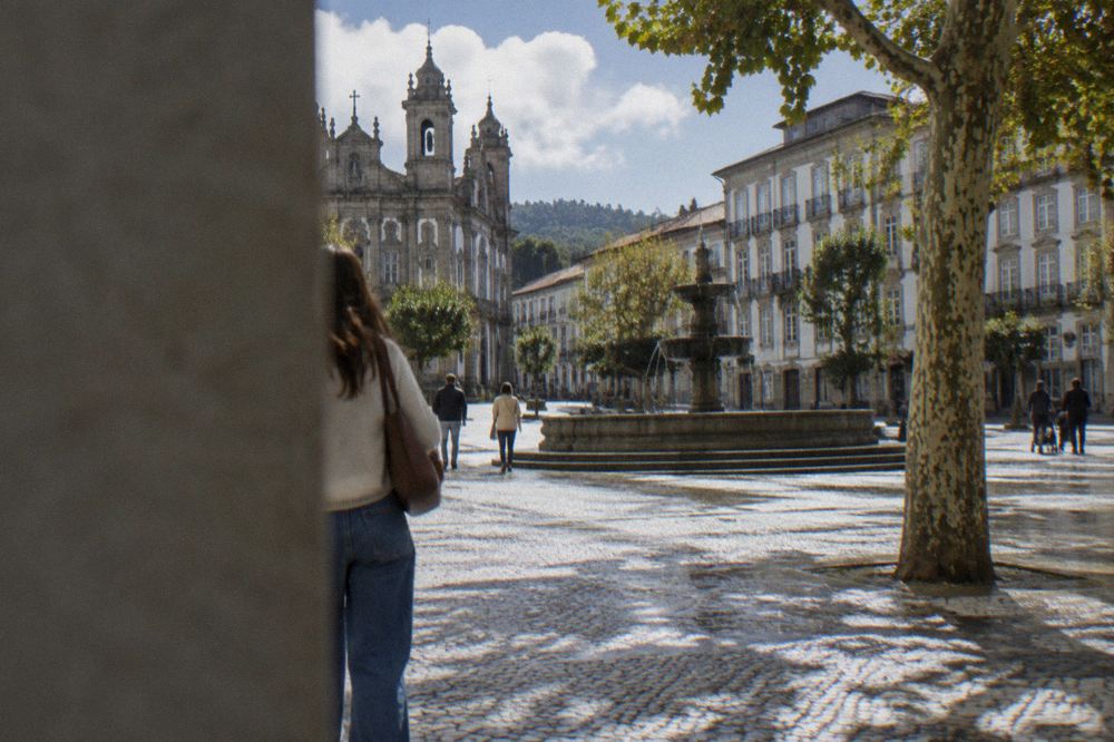 A visitor walking through a cobbled square in Braga's centre with a fountain and historic facades on a sunny morning
