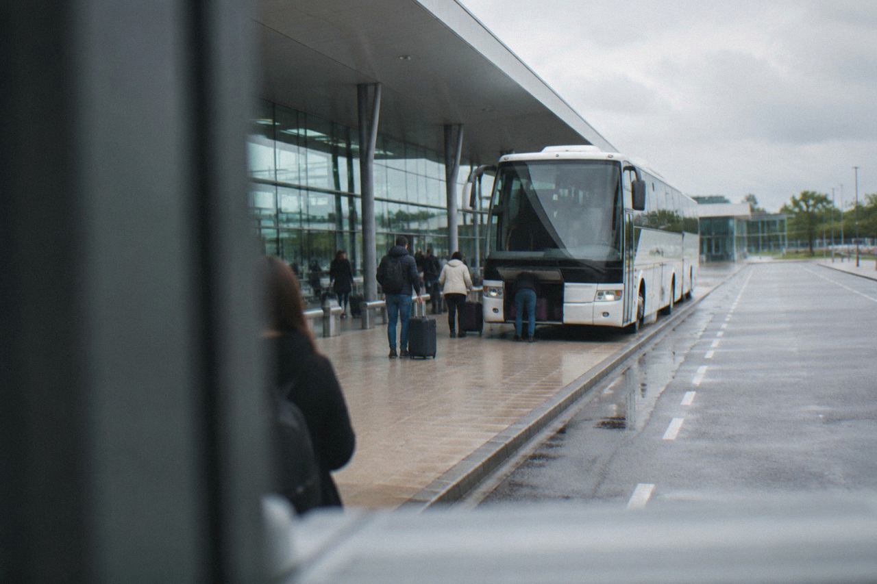 A coach parked at an airport terminal curb with passengers loading luggage